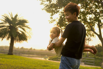 Side view of siblings standing on field against sky