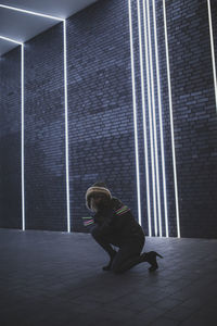 Full length of woman kneeling against illuminated lights on wall