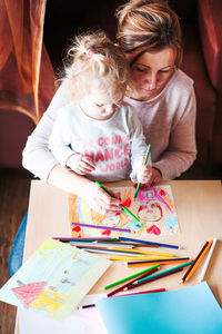 High angle view of mother and daughter painting on paper at home