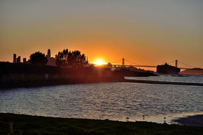 Silhouette bridge over river against sky during sunset