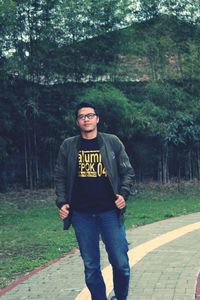 Portrait of young man standing against trees on footpath