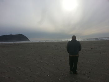 Rear view of man standing on beach against sky