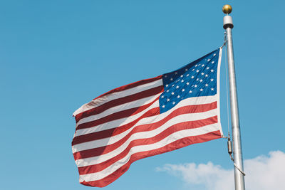 Low angle view of american flag fluttering against blue sky