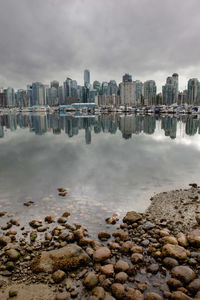 View of city at waterfront against cloudy sky