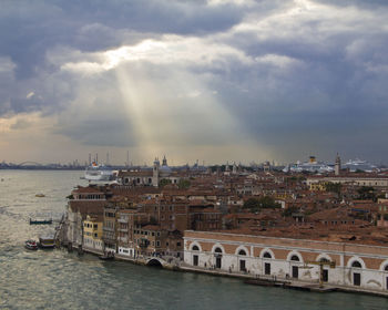 View of city at waterfront against cloudy sky