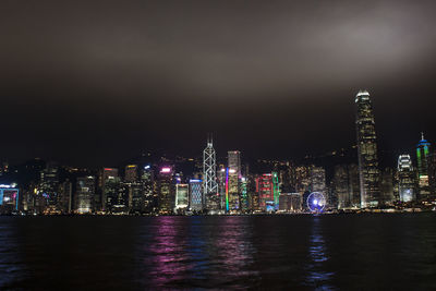 Illuminated buildings by river against sky at night