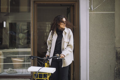 Female architect looking away while leaving with bicycle from office