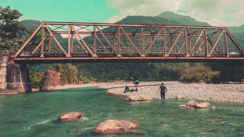 Rear view of man walking by river below bridge