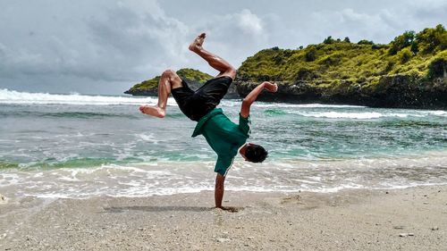 Full length of man practicing aerobatics on shore at beach