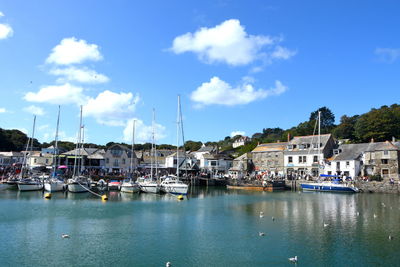 Sailboats moored in harbor by town against sky