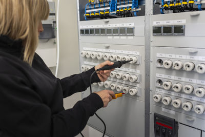 Female electrician with voltage tester repairing switchboard in meter room