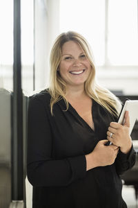 Portrait of happy businesswoman holding digital tablet in creative office