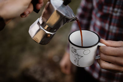 High angle of unrecognizable tourists with geyser coffee maker pouring hot coffee in metal mug while traveling in scottish highlands