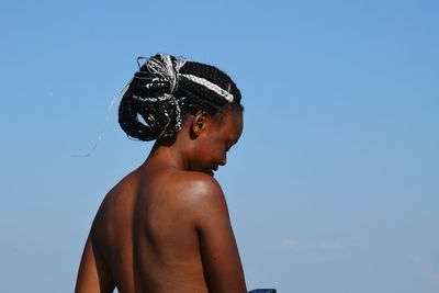 Shirtless woman standing against blue sky