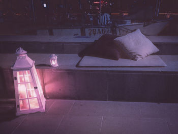 Illuminated electric lamp on sidewalk by street in city