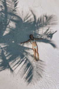 Aerial view of woman lying under tree shadow on sand