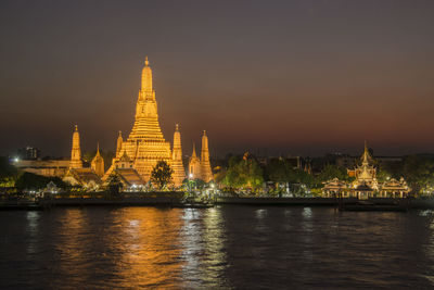 Illuminated temple building by river against sky