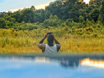 Rear view of man photographing from mobile phone against trees