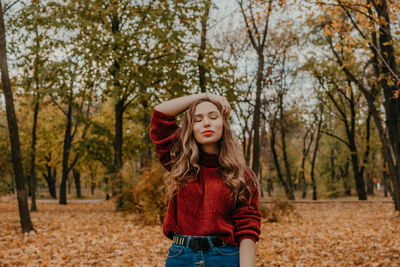 Young woman standing by tree in park during autumn