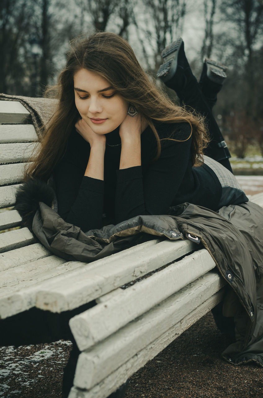 one person, young adult, young women, sitting, real people, lifestyles, leisure activity, hair, long hair, front view, beautiful woman, women, beauty, adult, day, tree, casual clothing, clothing, outdoors, hairstyle, teenager, contemplation, warm clothing