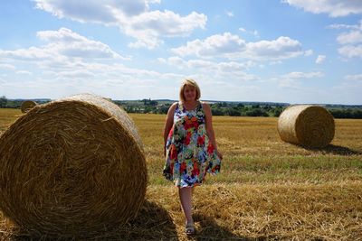 Full length of woman walking by hay bale against sky on agricultural field