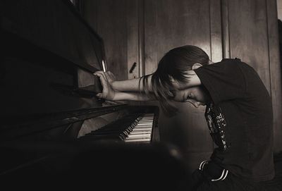 Side view of thoughtful boy sitting by piano at home
