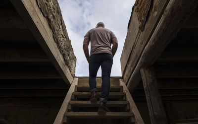 Rear view of adult man climbing up the wooden stairs, indoor toward the rooftop