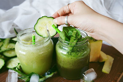 Cropped hand of woman inserting cucumber slice in smoothie