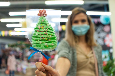 Close-up of woman wearing mask holding christmas tree shaped lollipop