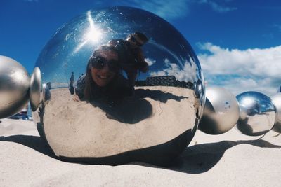 Happy man and woman at beach reflecting on metallic sphere