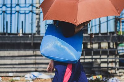 Midsection of woman holding umbrella standing against built structure