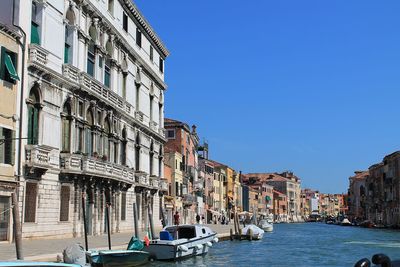 Boats in canal amidst buildings in city against clear blue sky