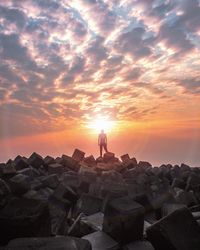 Man standing on rock by sea against sky during sunset