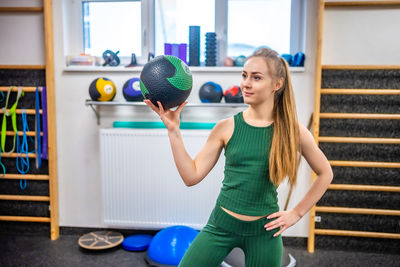 Portrait of smiling young woman lifting dumbbell in gym