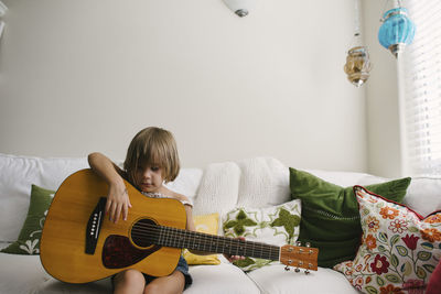 Girl playing guitar while sitting on sofa at home