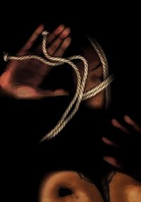 Close-up of hand holding rope against black background