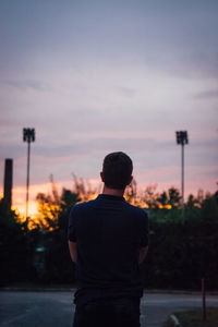 Rear view of man standing on street against sky during sunset