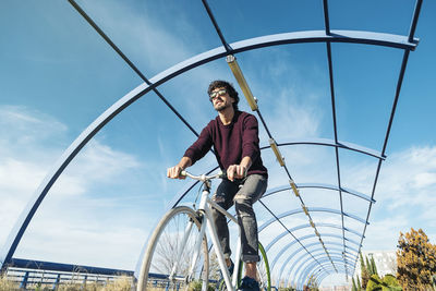 Low angle view of smiling man riding bicycle against sky