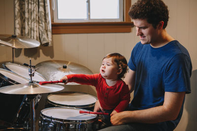 Cute boy playing drum while sitting with father at home