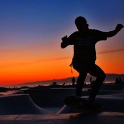 Silhouette man skateboarding on beach against orange sky