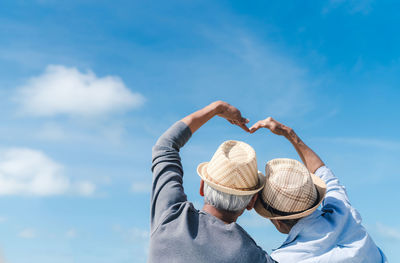 Rear view of woman holding hat against blue sky