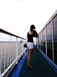 Rear view of woman standing on bridge against clear sky