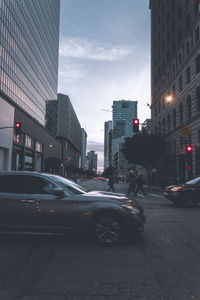 Cars on city street by buildings against sky