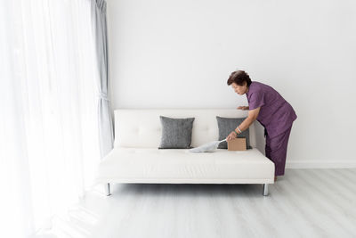 Side view of senior woman cleaning sofa on floor at home