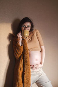 Pregnant woman holding her belly and drinking tea from mug.