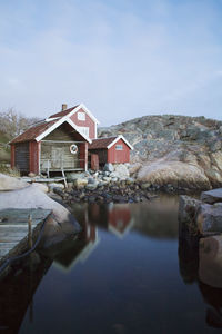 Boathouse on rocky shore against sky at sunset