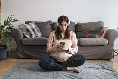 Young woman using phone while near sofa at home