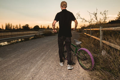 Portrait of man standing by bicycle against sky during sunset