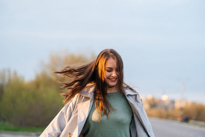 Beautiful smiling girl with long hair in a grey trench coat outdoors on the street spring