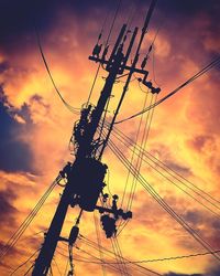 Low angle view of silhouette electricity pylon against dramatic sky